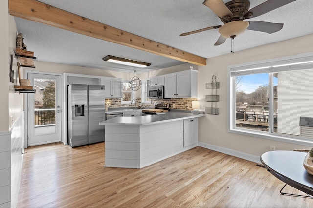 kitchen with light wood-style flooring, beamed ceiling, a peninsula, stainless steel appliances, and a textured ceiling