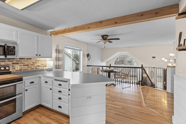 kitchen with a peninsula, white cabinetry, appliances with stainless steel finishes, and beamed ceiling