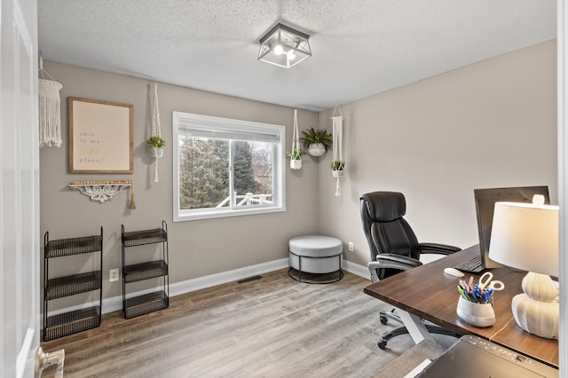 office space with a textured ceiling, wood finished floors, visible vents, baseboards, and heating unit