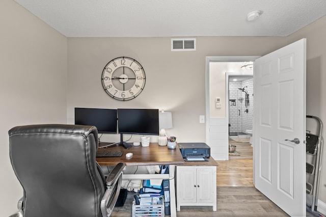 office with visible vents, a textured ceiling, and wood finished floors