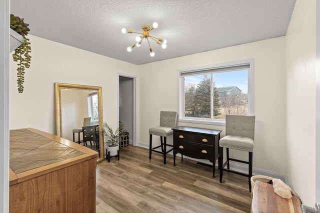 sitting room with a textured ceiling, baseboards, wood finished floors, and a notable chandelier