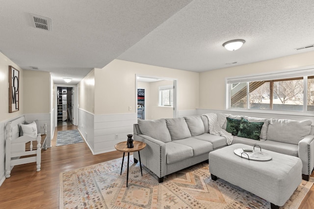 living area with a wealth of natural light, wainscoting, visible vents, and light wood-style floors