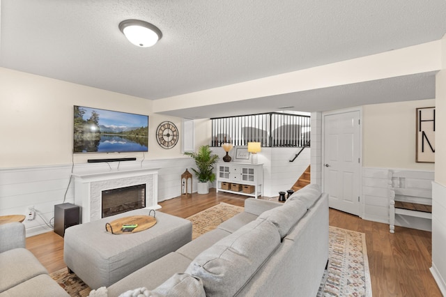 living room featuring wainscoting, wood finished floors, stairs, a textured ceiling, and a fireplace