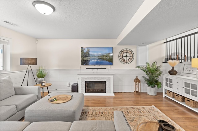 living area featuring a textured ceiling, a glass covered fireplace, wood finished floors, and wainscoting