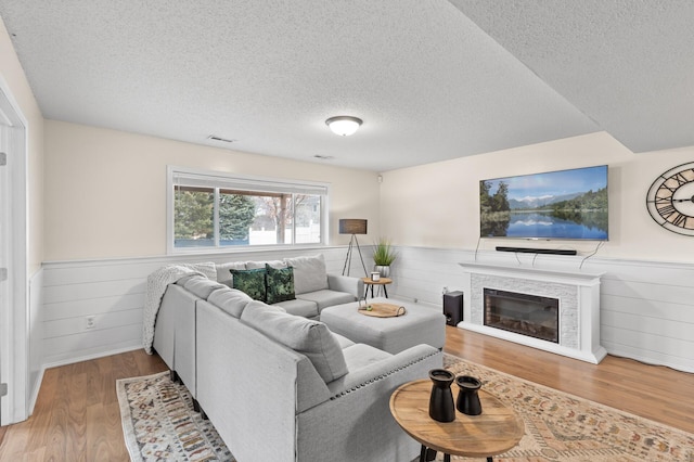 living room featuring a glass covered fireplace, wainscoting, and wood finished floors