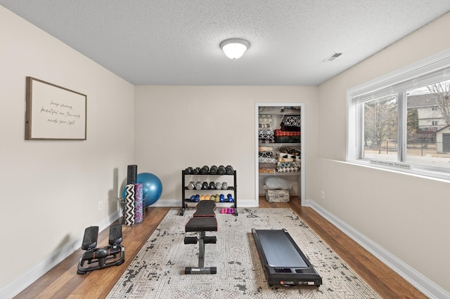 workout room with wood finished floors, visible vents, and baseboards