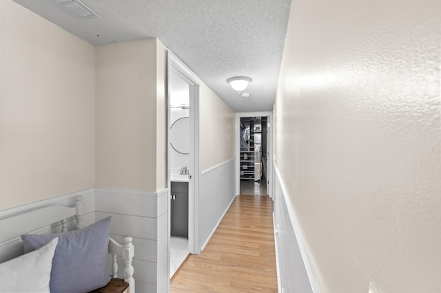 corridor featuring visible vents, wainscoting, a textured ceiling, light wood-type flooring, and a sink