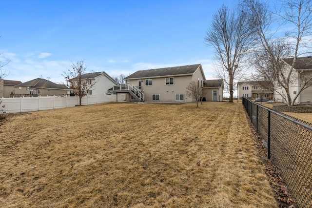 back of house with a fenced backyard, a residential view, a lawn, and stairs