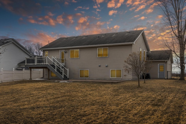 back of house at dusk featuring a yard, fence, a deck, and stairs