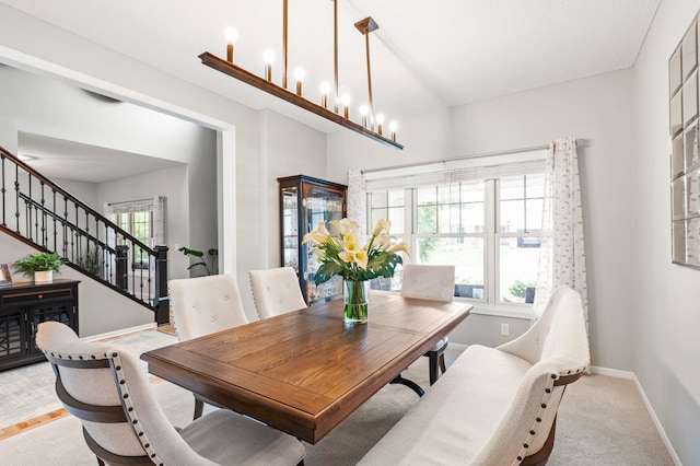 dining space with light carpet, an inviting chandelier, stairs, and baseboards