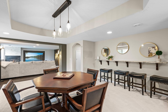 dining space featuring a large fireplace, arched walkways, a tray ceiling, carpet flooring, and recessed lighting