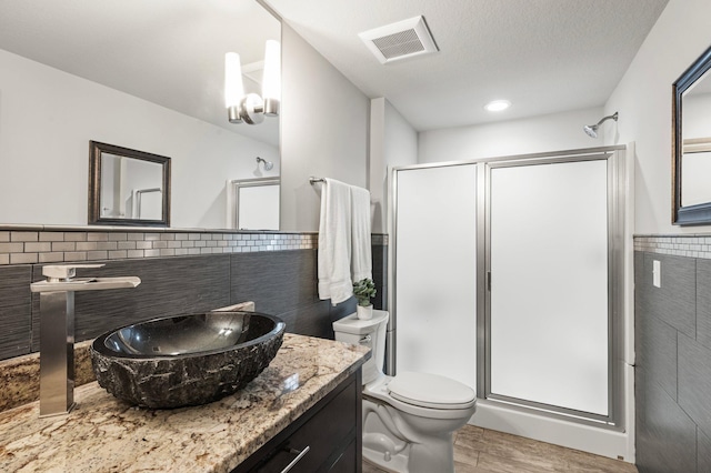 full bathroom featuring a wainscoted wall, a shower stall, visible vents, and tile walls