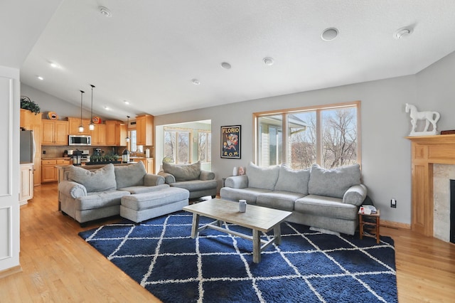 living area featuring lofted ceiling, light wood-style flooring, and a high end fireplace