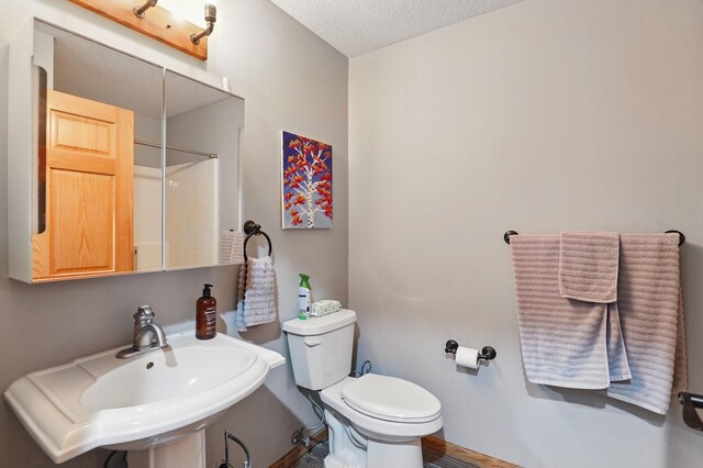 full bath with a sink, a shower, toilet, and a textured ceiling