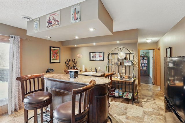 bar with visible vents, wet bar, freestanding refrigerator, a textured ceiling, and a sink