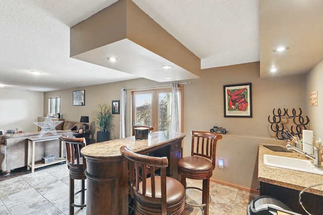 kitchen featuring a sink, light countertops, a textured ceiling, a kitchen bar, and open floor plan