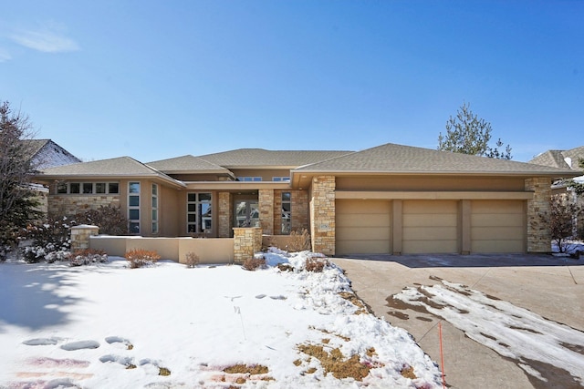 prairie-style home featuring an attached garage, stone siding, concrete driveway, and stucco siding