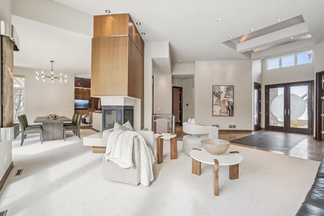 carpeted living area featuring french doors, a notable chandelier, visible vents, a towering ceiling, and a multi sided fireplace