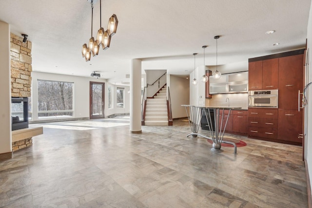 kitchen with glass insert cabinets, decorative light fixtures, oven, a textured ceiling, and a fireplace