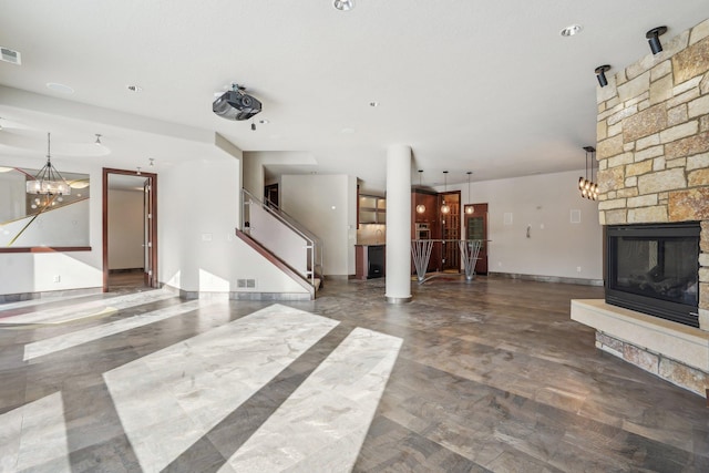 unfurnished living room featuring stairs, visible vents, a stone fireplace, and an inviting chandelier