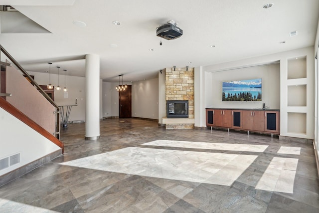 unfurnished living room featuring baseboards, visible vents, stairway, a fireplace, and a chandelier