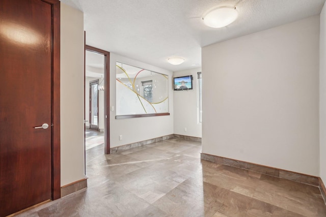 spare room featuring a textured ceiling and baseboards