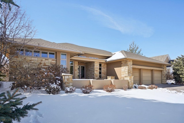 prairie-style house with a garage, stone siding, a fenced front yard, and stucco siding