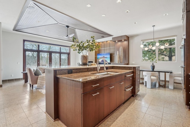 9730 Sky Ln, Eden Prairie, MN 55347 - kitchen with baseboards, a kitchen island with sink, a sink, dark stone counters, and decorative light fixtures