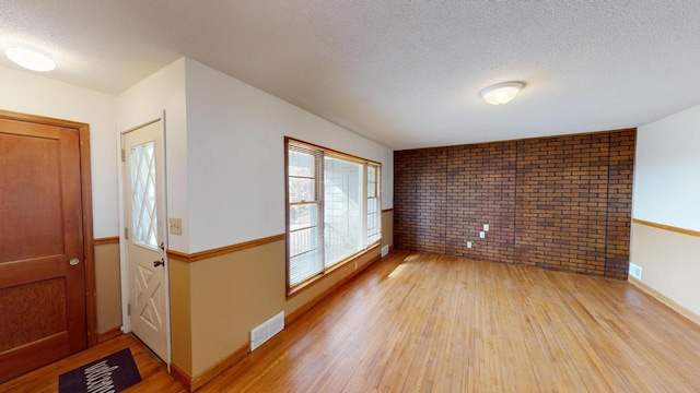 interior space featuring brick wall, light wood-style flooring, visible vents, and a textured ceiling