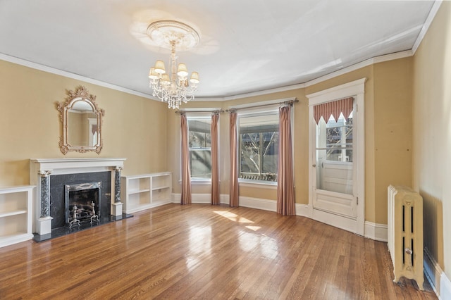 unfurnished living room featuring crown molding, a fireplace, radiator heating unit, an inviting chandelier, and wood finished floors