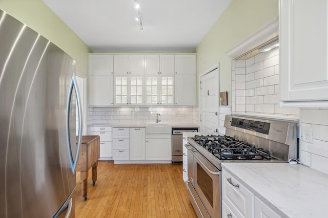 kitchen featuring light wood-type flooring, tasteful backsplash, appliances with stainless steel finishes, and white cabinets