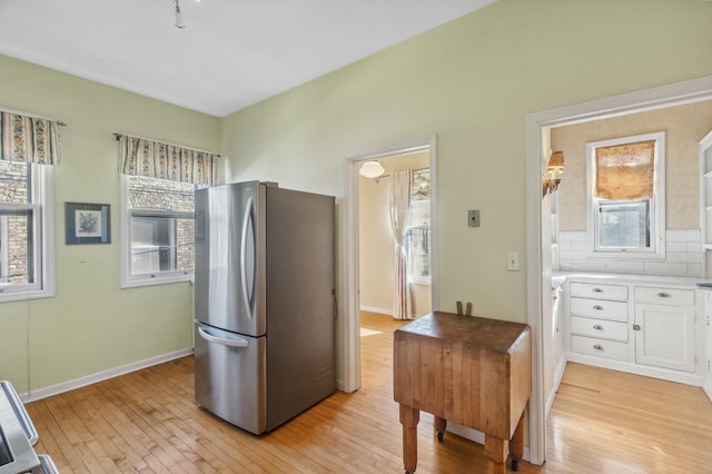 kitchen with light wood finished floors, baseboards, white cabinets, decorative backsplash, and freestanding refrigerator