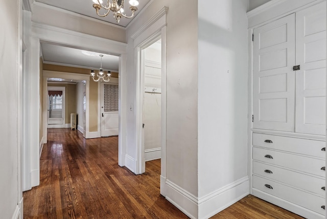 hall with dark wood-style flooring, crown molding, radiator heating unit, a chandelier, and baseboards