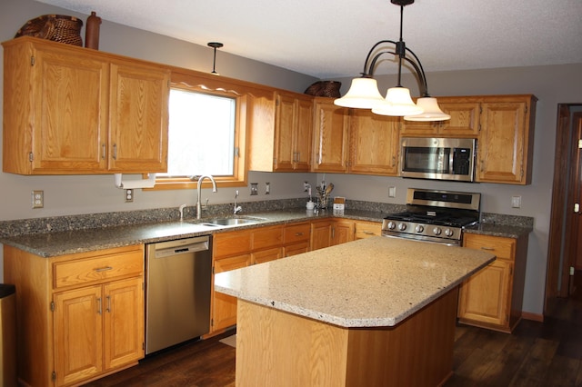 kitchen with dark wood-type flooring, a sink, appliances with stainless steel finishes, a center island, and pendant lighting