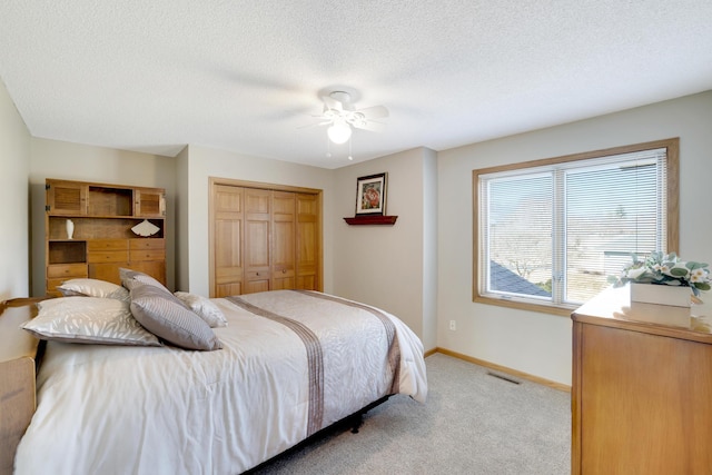 bedroom featuring a closet, visible vents, light carpet, a textured ceiling, and baseboards