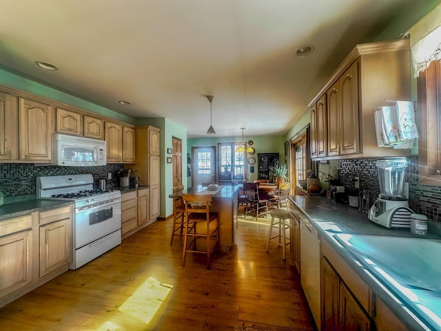 kitchen with light wood-style flooring, white appliances, a kitchen island, backsplash, and a kitchen bar