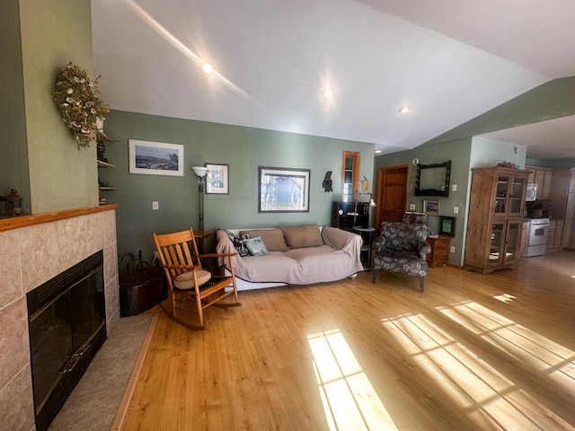 living area featuring vaulted ceiling, light wood finished floors, and a tile fireplace