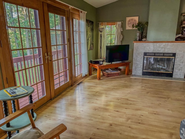 interior space with visible vents, a tile fireplace, lofted ceiling, wood finished floors, and french doors