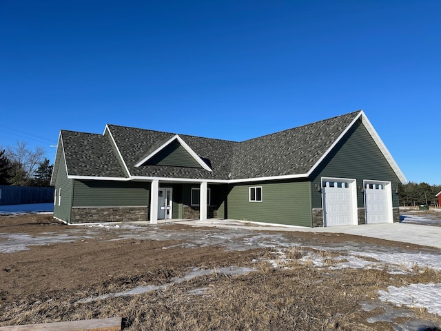 view of front facade with a garage, stone siding, a porch, and roof with shingles