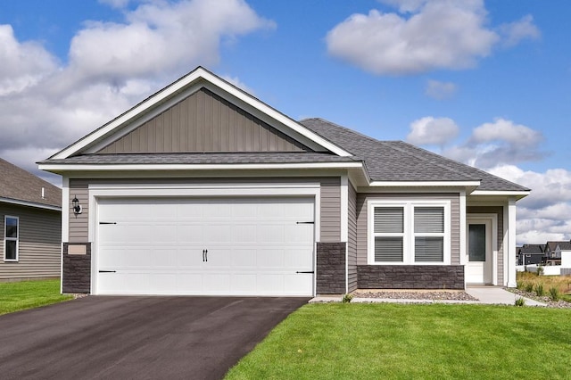 view of front of house with aphalt driveway, stone siding, a front yard, and roof with shingles