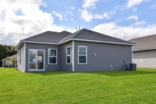 rear view of property featuring central air condition unit, a shingled roof, and a lawn