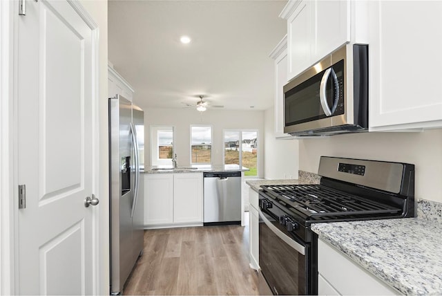 kitchen with light stone counters, light wood-type flooring, appliances with stainless steel finishes, and white cabinets