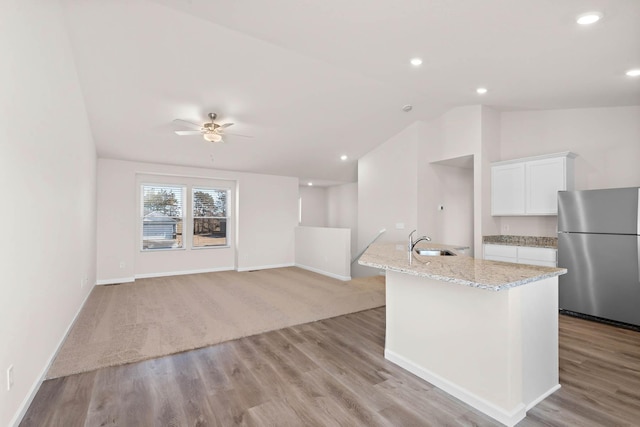 kitchen with a sink, freestanding refrigerator, white cabinets, lofted ceiling, and light stone countertops