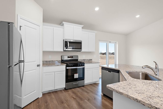 kitchen with light stone countertops, wood finished floors, a sink, appliances with stainless steel finishes, and white cabinetry