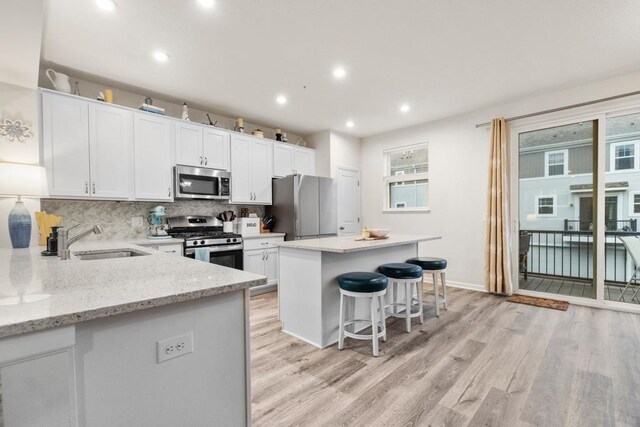 kitchen featuring a sink, white cabinets, appliances with stainless steel finishes, light wood finished floors, and tasteful backsplash