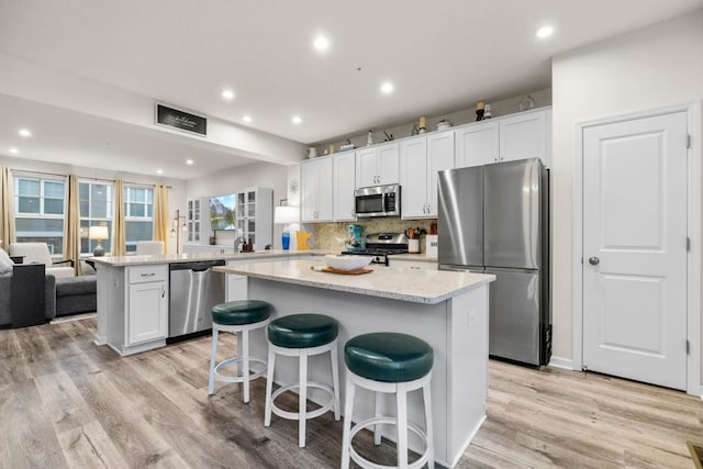 kitchen with stainless steel appliances, white cabinets, light wood-type flooring, a center island, and tasteful backsplash