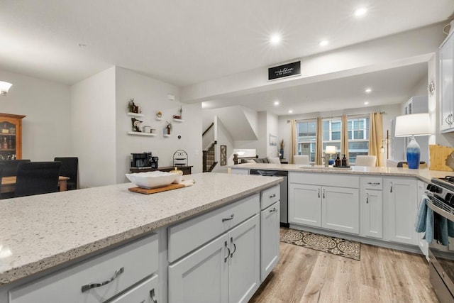 kitchen with light wood finished floors, white cabinets, appliances with stainless steel finishes, light stone counters, and a peninsula