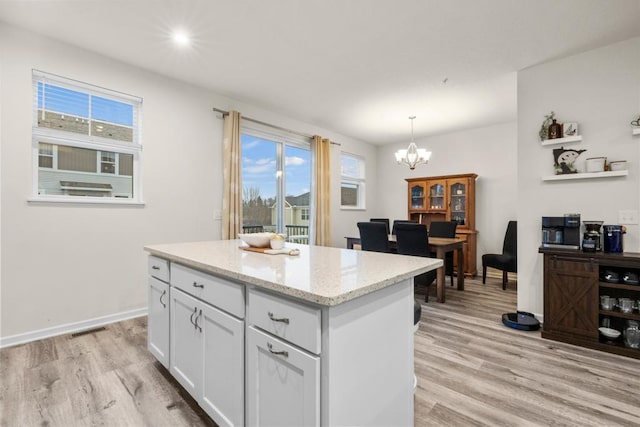 kitchen with a notable chandelier, visible vents, white cabinets, light wood-type flooring, and a center island