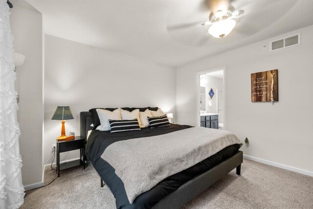 bedroom featuring light colored carpet, visible vents, ceiling fan, ensuite bath, and baseboards