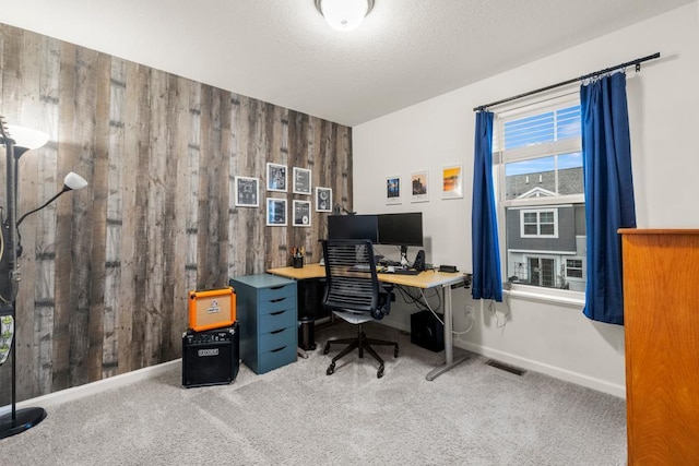 carpeted home office with baseboards, wooden walls, visible vents, and a textured ceiling